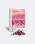 A puzzle box with a vibrant image of flamingos on one leg in a pink hue during sunset, and a pile of pink puzzle pieces in front.